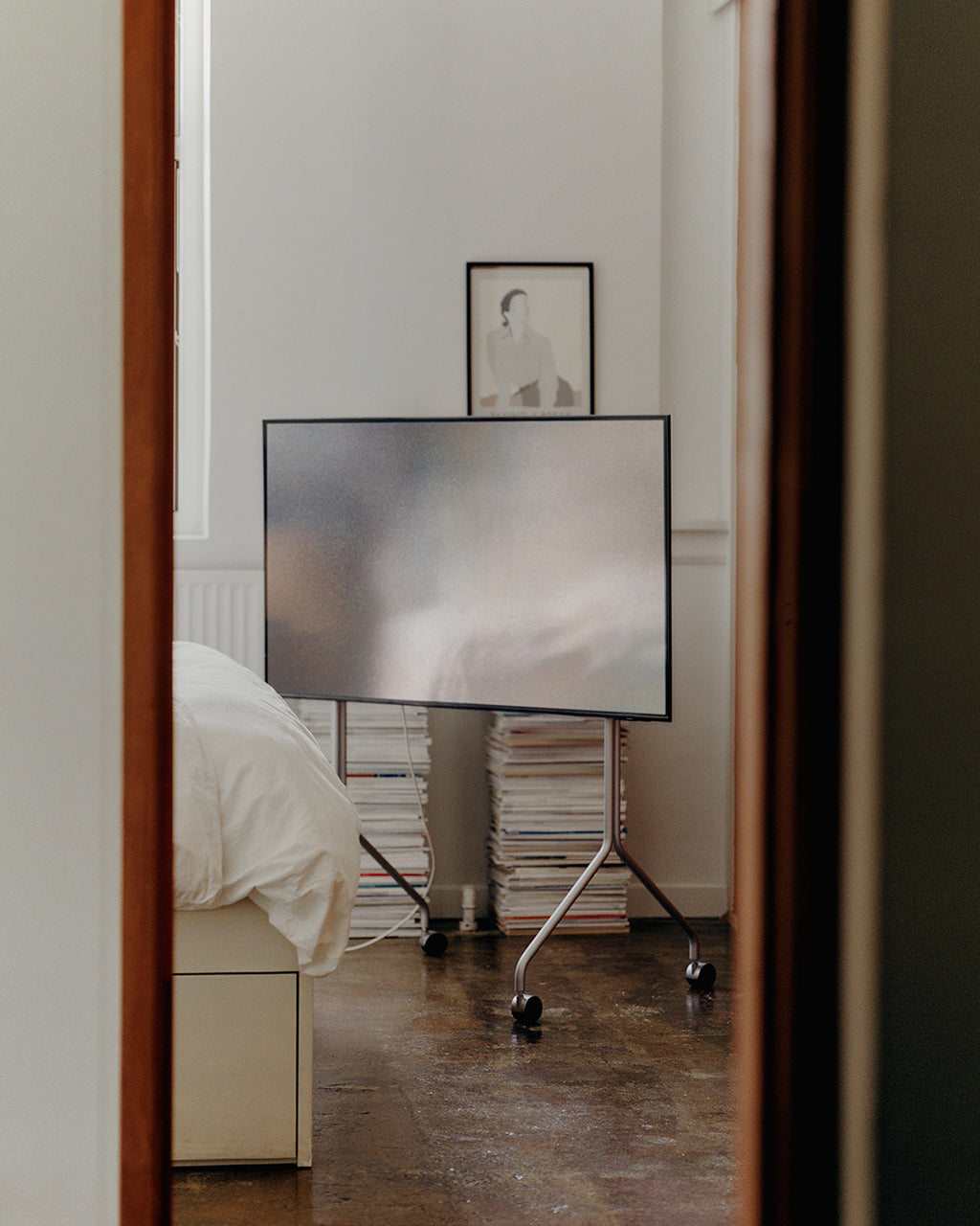 Moon Tall in Cloudy Silver con TV in camera da letto, vista attraverso una porta, ruote visibili sul pavimento